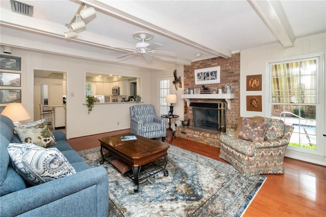 living area featuring a brick fireplace, wood finished floors, visible vents, and plenty of natural light