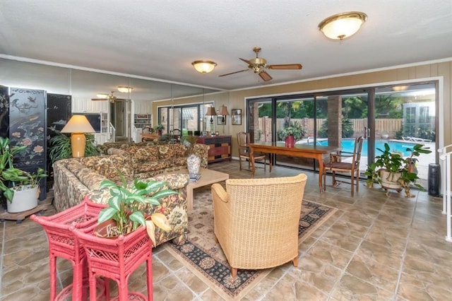 living room featuring ornamental molding, a ceiling fan, stone finish floor, and plenty of natural light