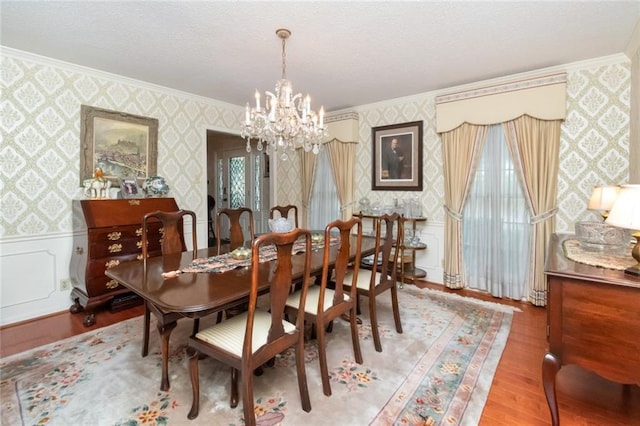 dining area featuring a notable chandelier, ornamental molding, wood finished floors, and wallpapered walls