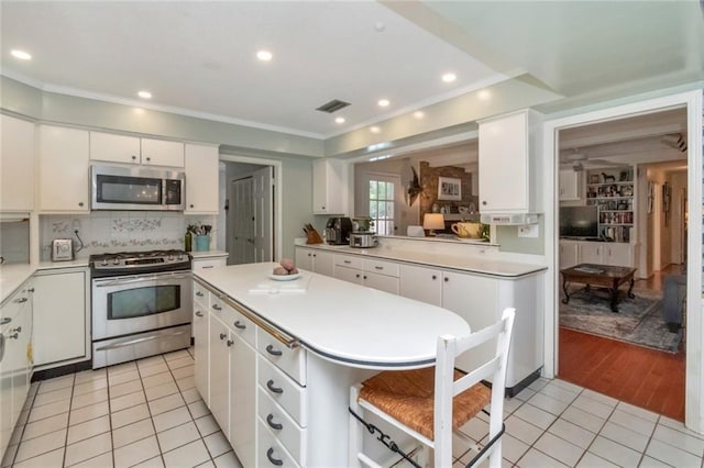 kitchen featuring white cabinets, stainless steel appliances, light countertops, light tile patterned floors, and a center island