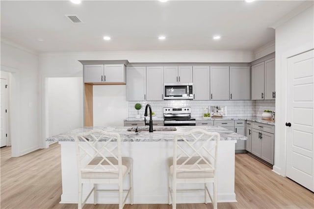 kitchen with light stone counters, stainless steel appliances, and an island with sink