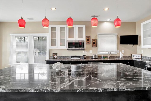 kitchen featuring white cabinetry, hanging light fixtures, and dark stone counters