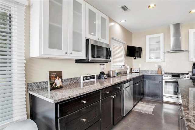 kitchen with appliances with stainless steel finishes, wall chimney exhaust hood, sink, and white cabinets