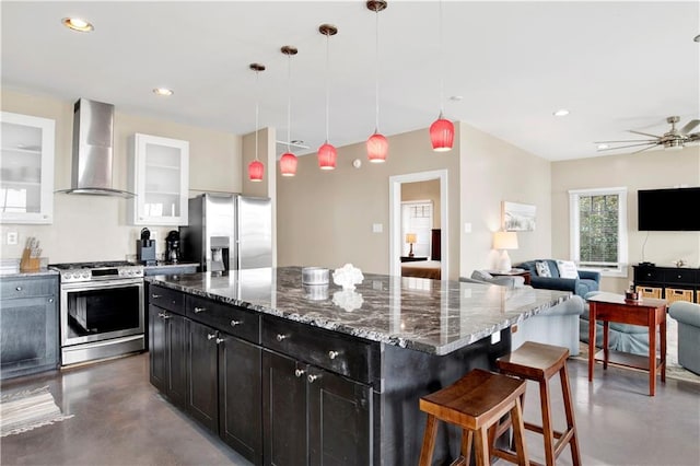 kitchen with stone counters, white cabinetry, appliances with stainless steel finishes, a center island, and wall chimney exhaust hood