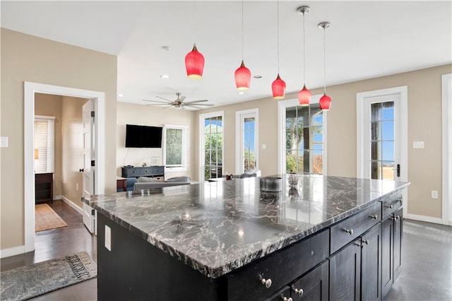 kitchen with ceiling fan, dark stone counters, hanging light fixtures, and a kitchen island