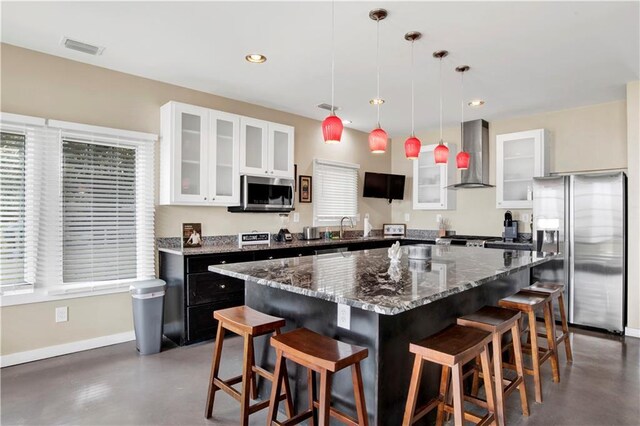 kitchen featuring wall chimney exhaust hood, sink, a kitchen island, pendant lighting, and stainless steel appliances