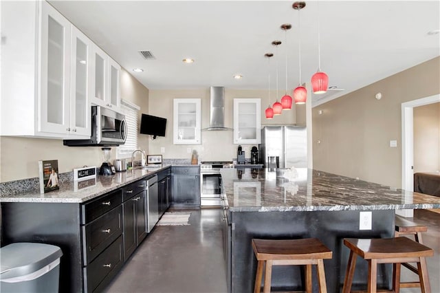 kitchen featuring wall chimney exhaust hood, sink, white cabinetry, hanging light fixtures, and stainless steel appliances