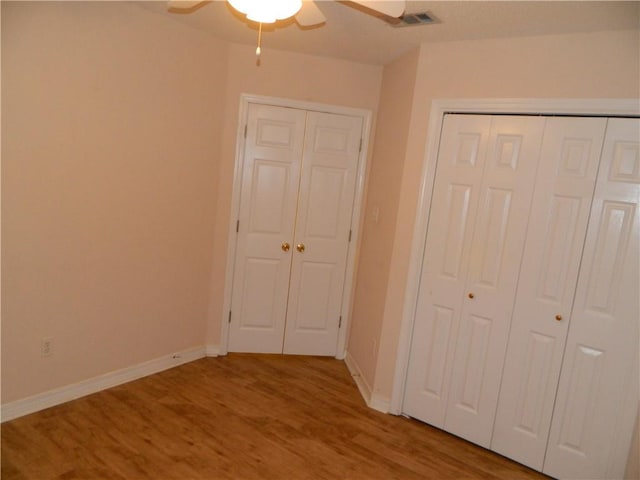 unfurnished bedroom with multiple closets, ceiling fan, and hardwood / wood-style floors