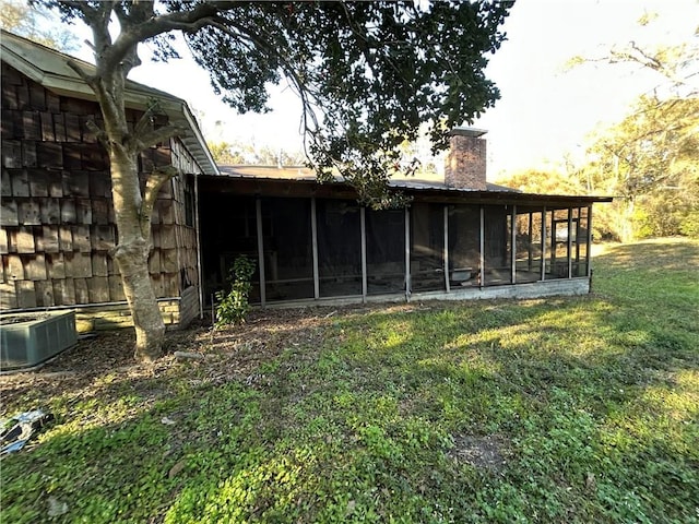 rear view of property featuring central air condition unit, a lawn, a chimney, and a sunroom