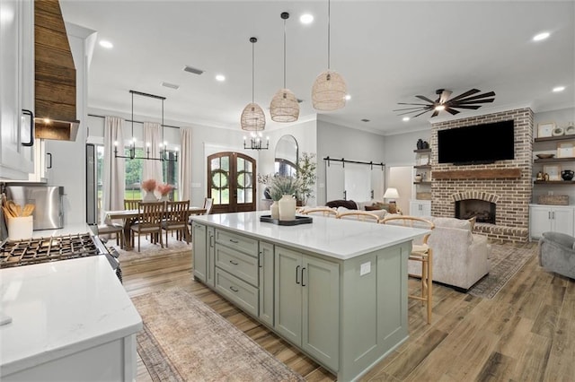 kitchen with hanging light fixtures, ceiling fan with notable chandelier, green cabinetry, a fireplace, and crown molding