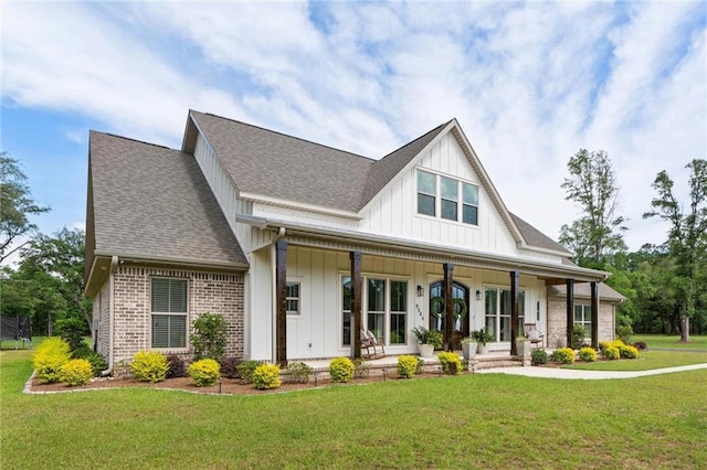modern farmhouse style home with covered porch, a shingled roof, board and batten siding, a front yard, and brick siding