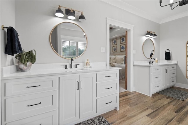 ensuite bathroom with a sink, wood finished floors, ornamental molding, connected bathroom, and two vanities