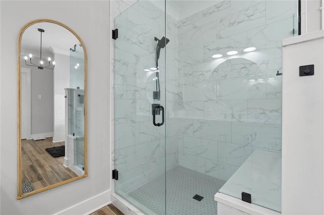 bathroom with baseboards, a shower stall, a notable chandelier, and wood finished floors