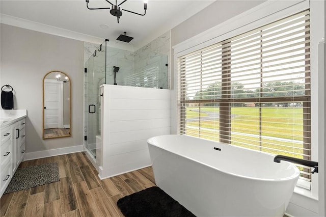 bathroom with an inviting chandelier, wood finished floors, a stall shower, a freestanding bath, and vanity