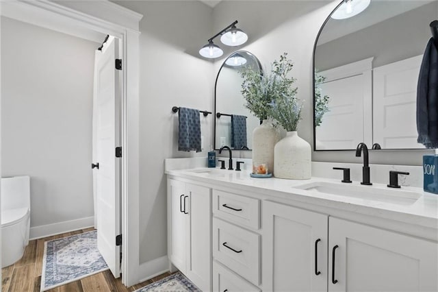 full bathroom with a sink, double vanity, baseboards, and wood finished floors