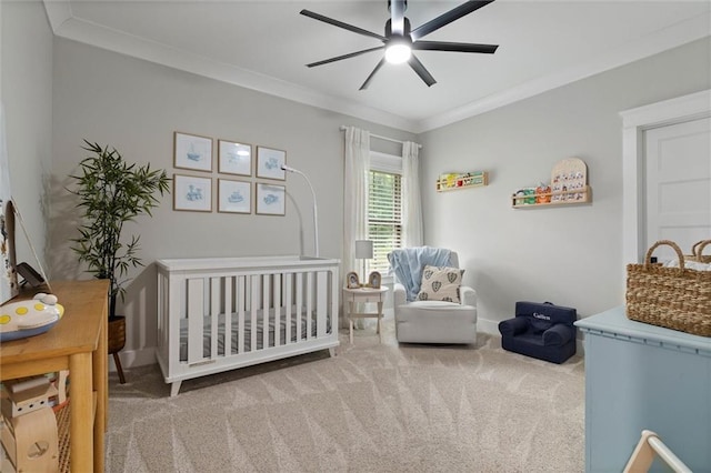 carpeted bedroom with crown molding, a nursery area, baseboards, and a ceiling fan