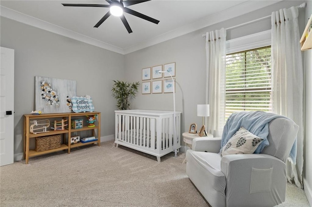 bedroom featuring a crib, ornamental molding, ceiling fan, and carpet