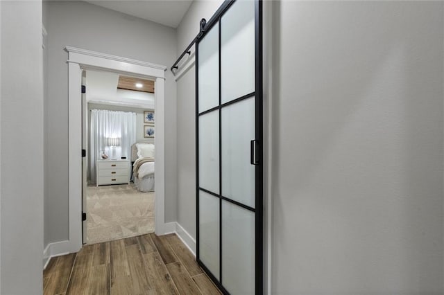 corridor featuring dark wood-style flooring, a barn door, and baseboards