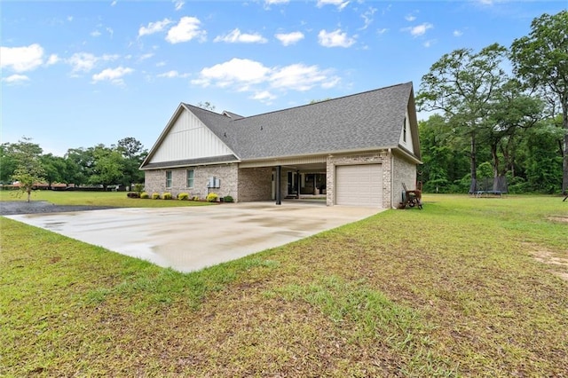 back of house with a lawn, a trampoline, brick siding, and driveway
