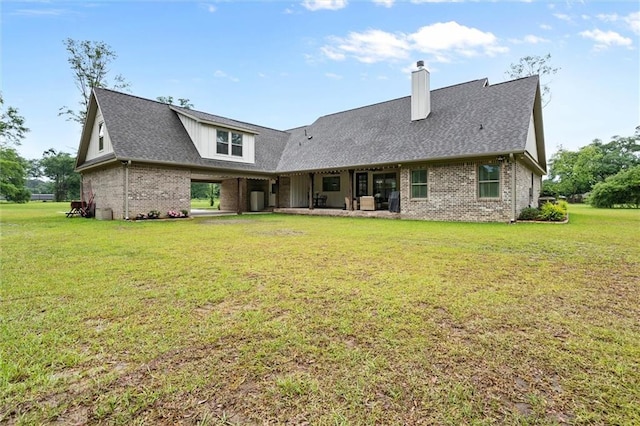 back of property with roof with shingles, a chimney, brick siding, and a lawn