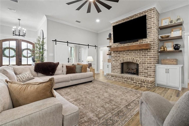 living room featuring french doors, a barn door, ceiling fan with notable chandelier, crown molding, and light wood-style floors