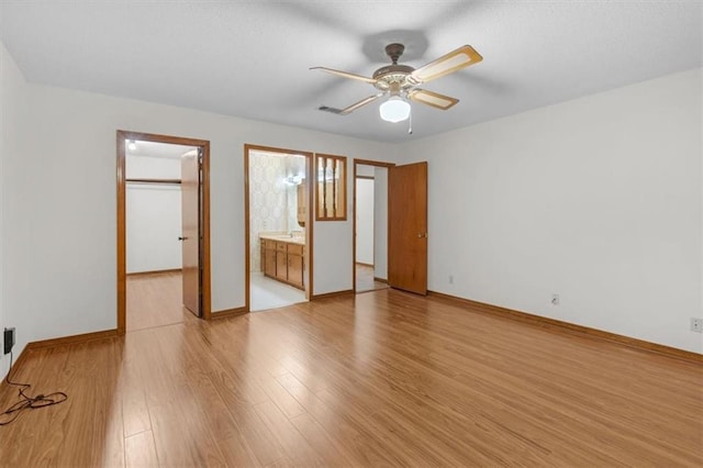 unfurnished bedroom featuring a closet, light hardwood / wood-style flooring, connected bathroom, a walk in closet, and ceiling fan