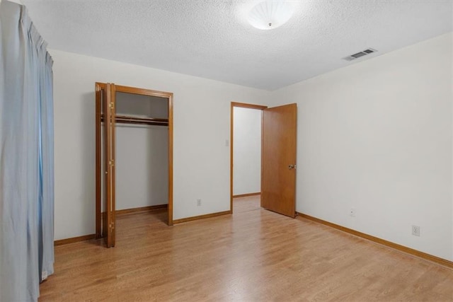 unfurnished bedroom featuring a textured ceiling, light hardwood / wood-style floors, and a closet