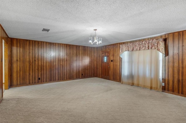 carpeted spare room featuring a textured ceiling, wood walls, and a chandelier