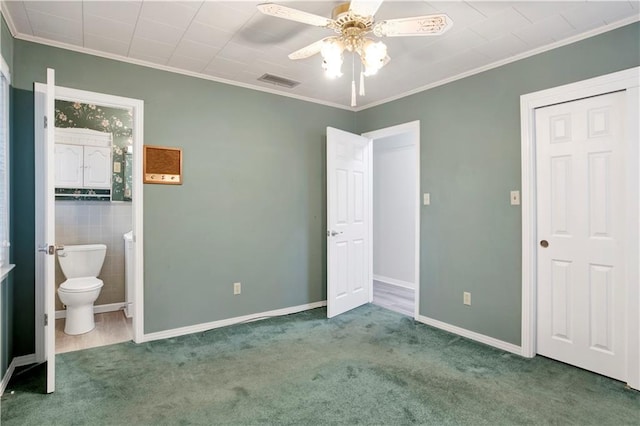 unfurnished bedroom featuring ensuite bathroom, ceiling fan, carpet flooring, and crown molding