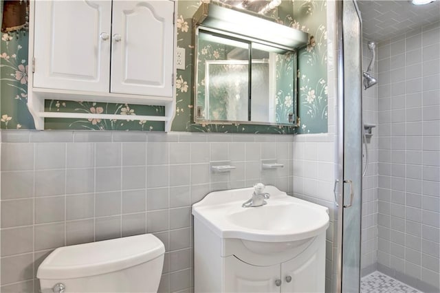 bathroom featuring toilet, vanity, tile walls, and a shower with shower door