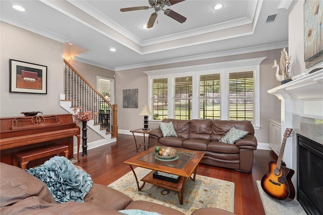 living room with ceiling fan, a raised ceiling, dark hardwood / wood-style flooring, crown molding, and a fireplace