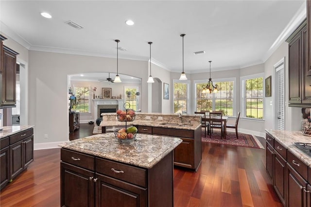 kitchen featuring a center island, sink, hanging light fixtures, ornamental molding, and dark brown cabinets