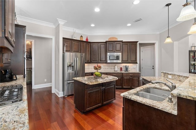 kitchen featuring light stone countertops, sink, stainless steel appliances, pendant lighting, and a kitchen island