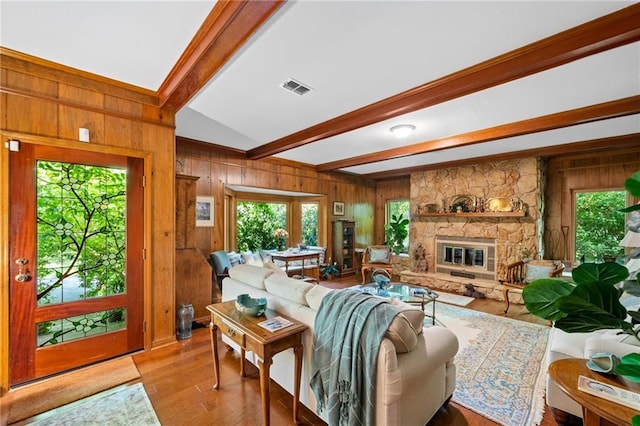 living room with wood walls, light hardwood / wood-style flooring, lofted ceiling with beams, and a stone fireplace