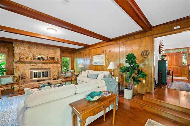 living room featuring beamed ceiling, a stone fireplace, dark wood-type flooring, and wooden walls