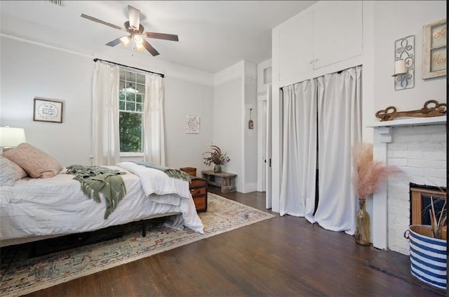 bedroom featuring a fireplace, ceiling fan, and dark wood-type flooring