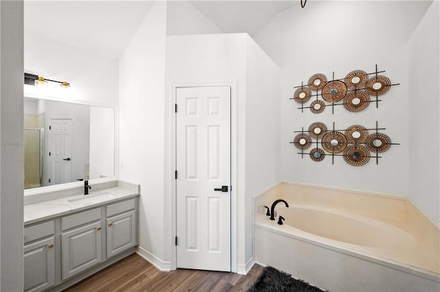 bathroom featuring vanity, a tub to relax in, hardwood / wood-style flooring, and lofted ceiling