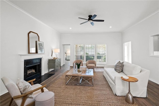 living room featuring a tiled fireplace, dark wood-type flooring, ornamental molding, and ceiling fan