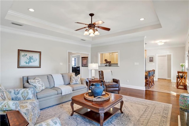 living room featuring hardwood / wood-style flooring, a tray ceiling, crown molding, and ceiling fan