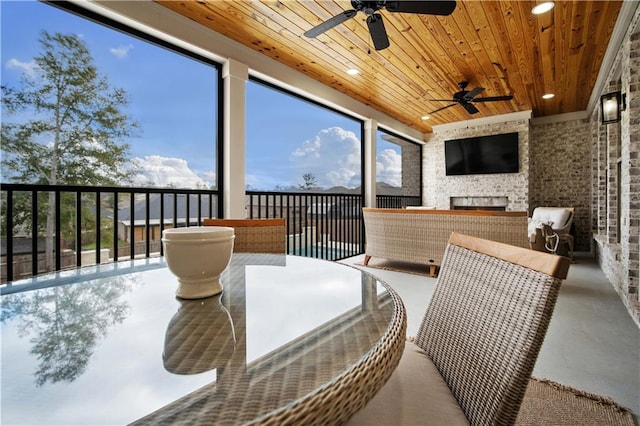 sunroom / solarium with an outdoor stone fireplace, ceiling fan, and wood ceiling