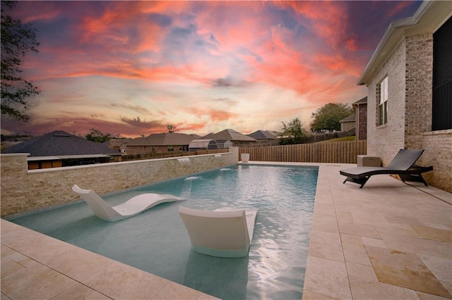 pool at dusk featuring pool water feature, a patio area, and a water slide