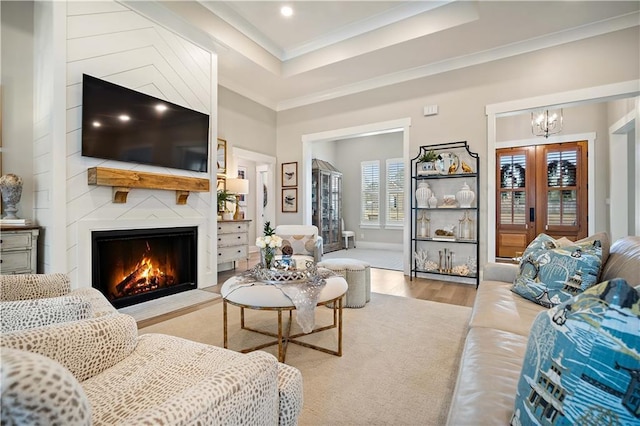 living room featuring a large fireplace, an inviting chandelier, a raised ceiling, light wood-type flooring, and ornamental molding