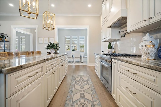 kitchen with light stone counters, backsplash, pendant lighting, high end range, and custom exhaust hood