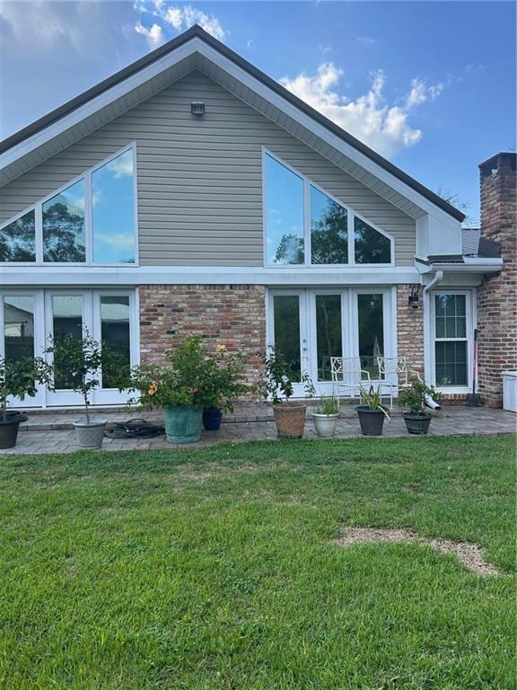 back of house featuring a yard, french doors, brick siding, and a chimney