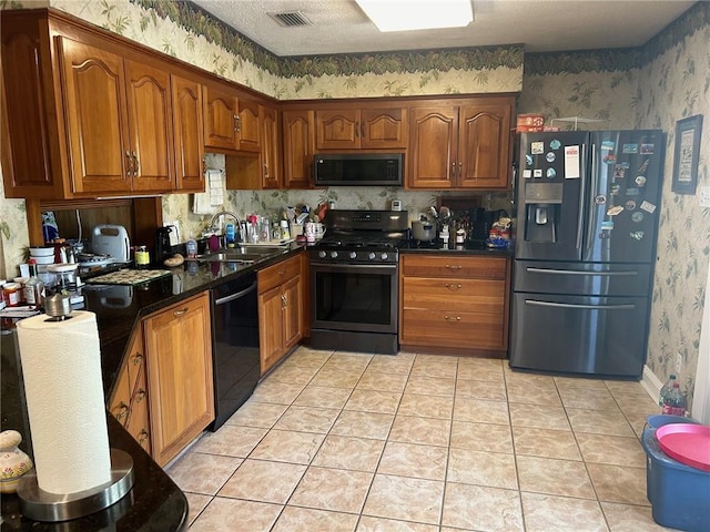 kitchen with dark stone counters, black appliances, light tile patterned flooring, and sink