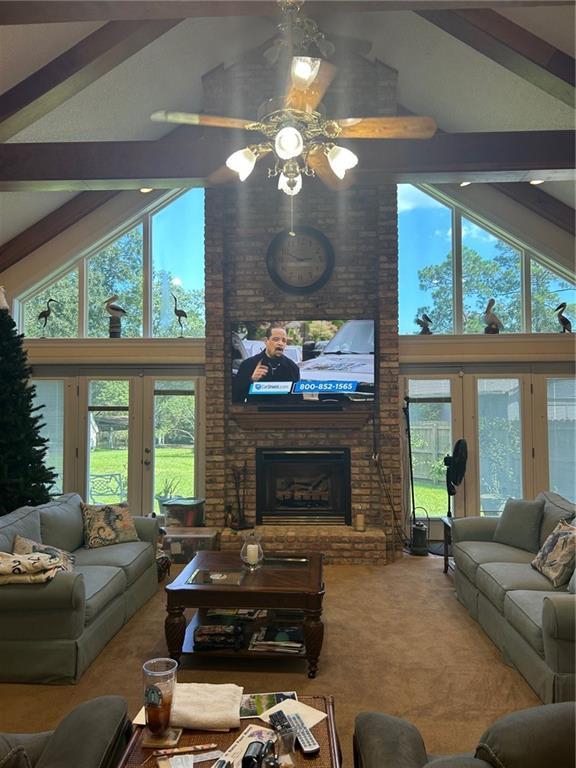 carpeted living area featuring french doors, beamed ceiling, a brick fireplace, and a healthy amount of sunlight