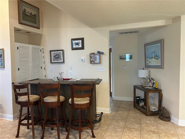bar featuring baseboards, light tile patterned floors, a textured ceiling, a bar, and visible vents