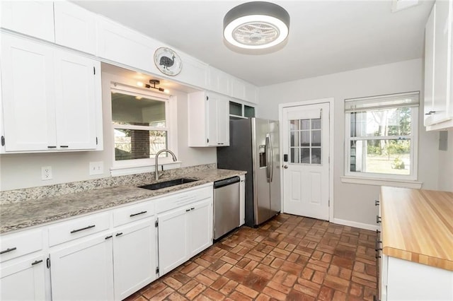 kitchen with a sink, appliances with stainless steel finishes, brick floor, and white cabinetry