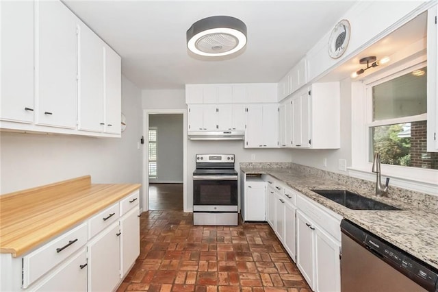 kitchen with a sink, under cabinet range hood, white cabinetry, appliances with stainless steel finishes, and brick floor