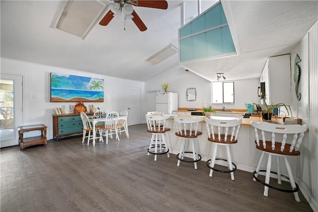 kitchen with kitchen peninsula, dark hardwood / wood-style flooring, lofted ceiling, white refrigerator, and a breakfast bar